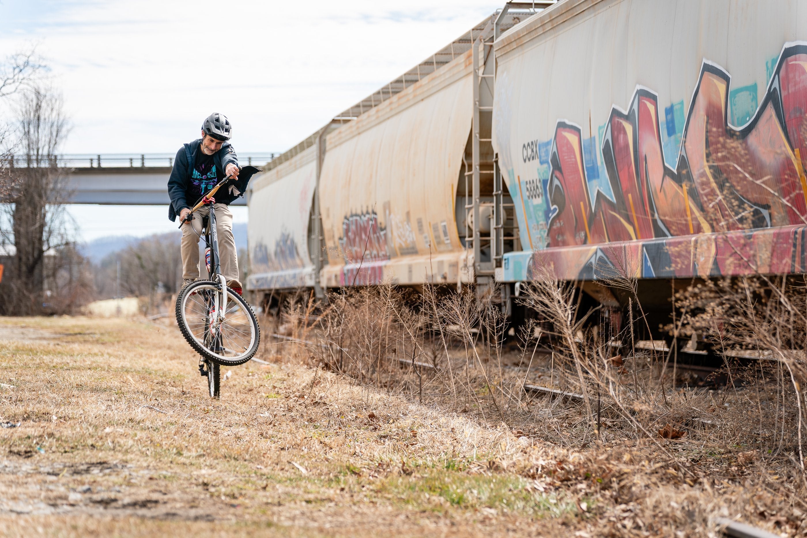 Seth Alvo on a penny-farthing by a graffiti train